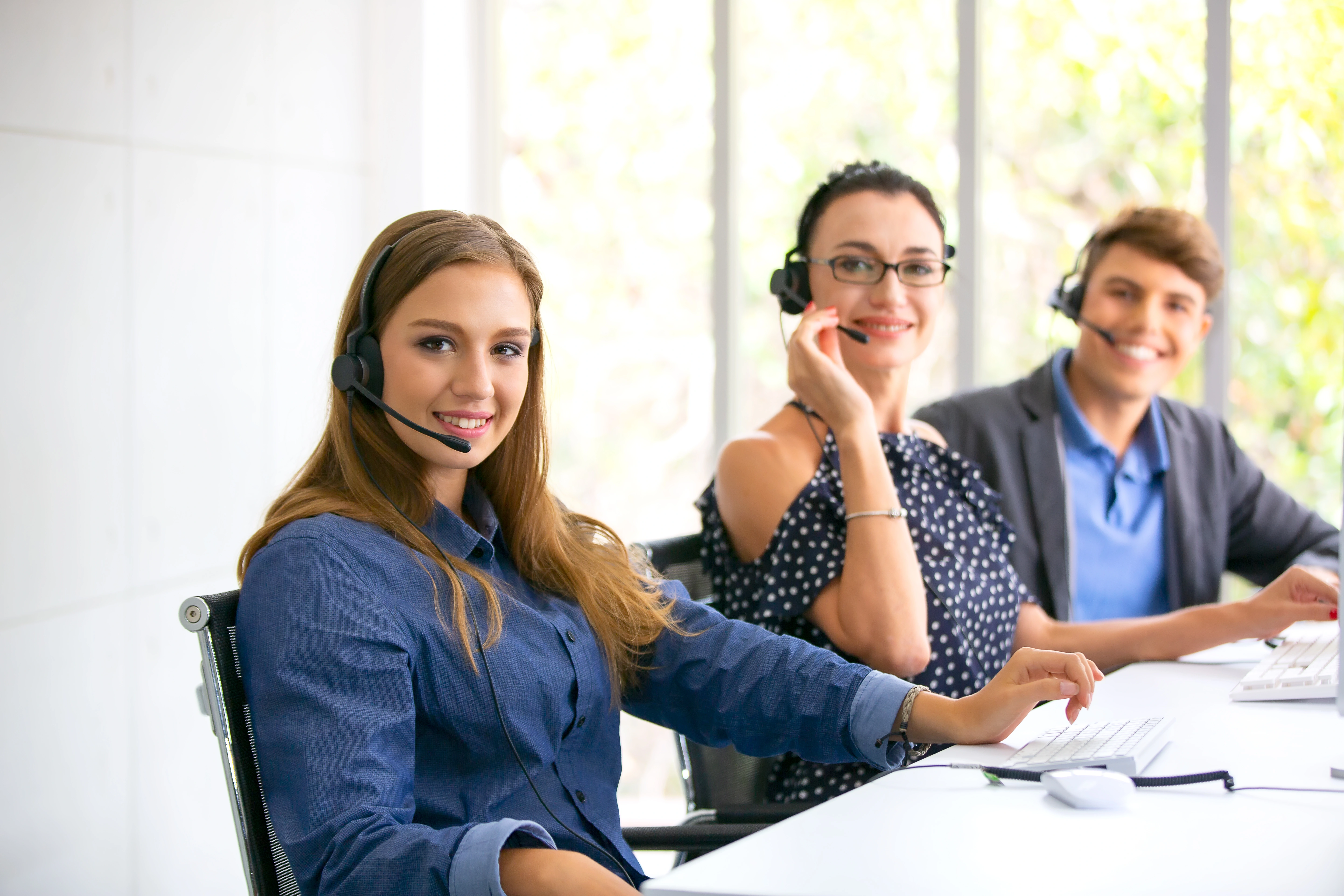 A group of call representatives wearing headsets and smiling at the camera. They have keyboards in front of them.