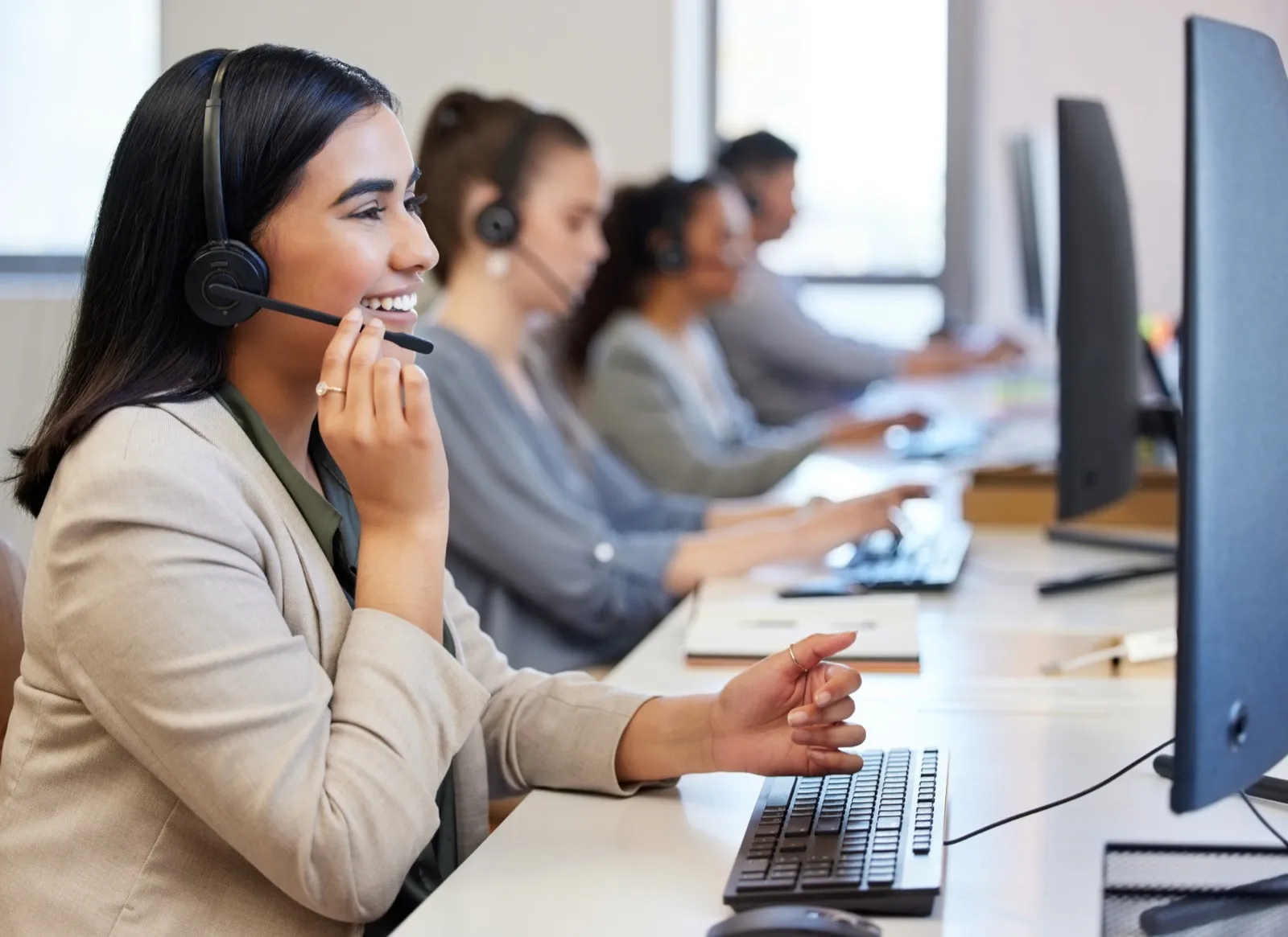 A woman sitting at a computer talking into a headset. She is smiling while looking at the computer.