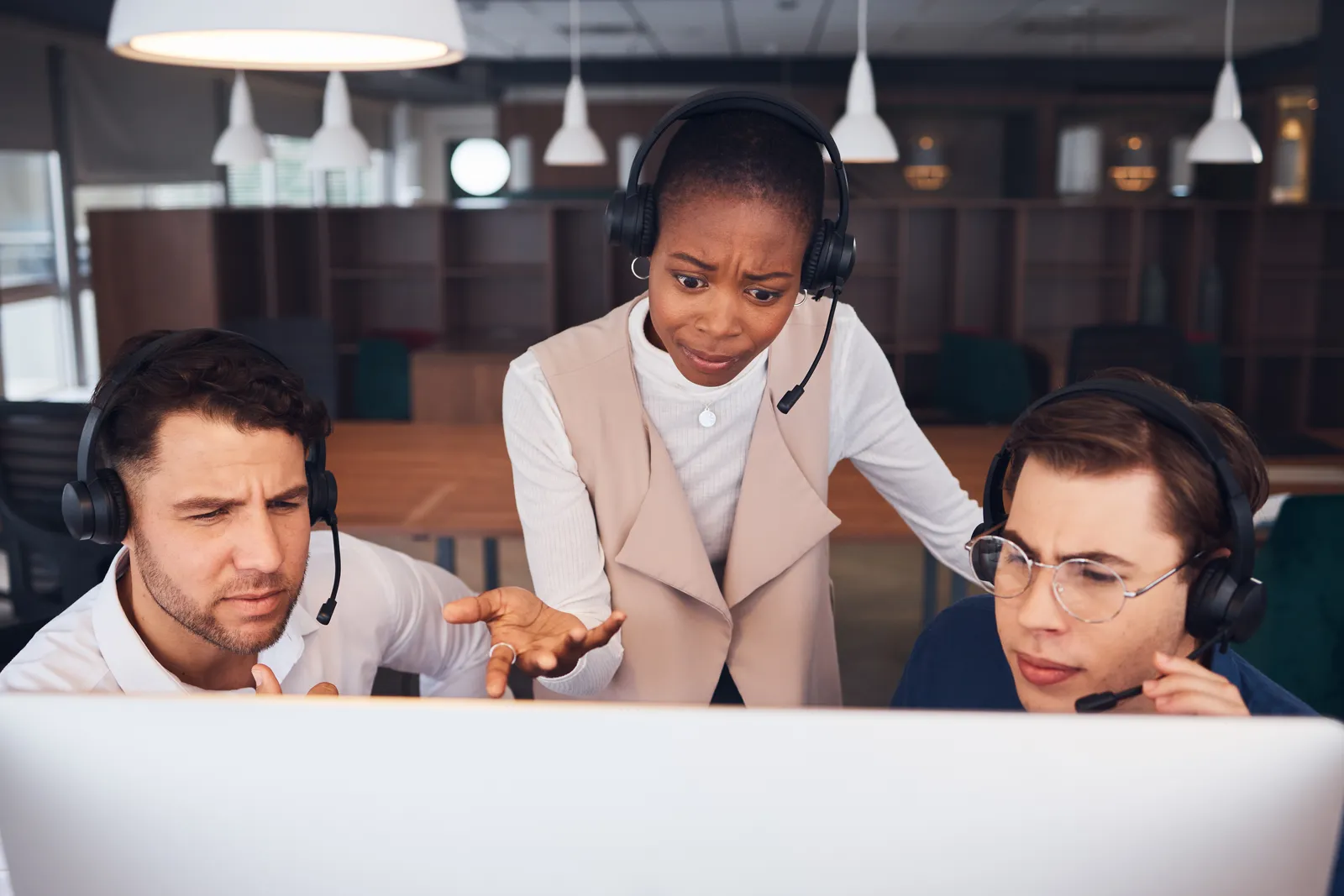 A group of puzzled call agents looking at the computer. They are all wearing headsets.