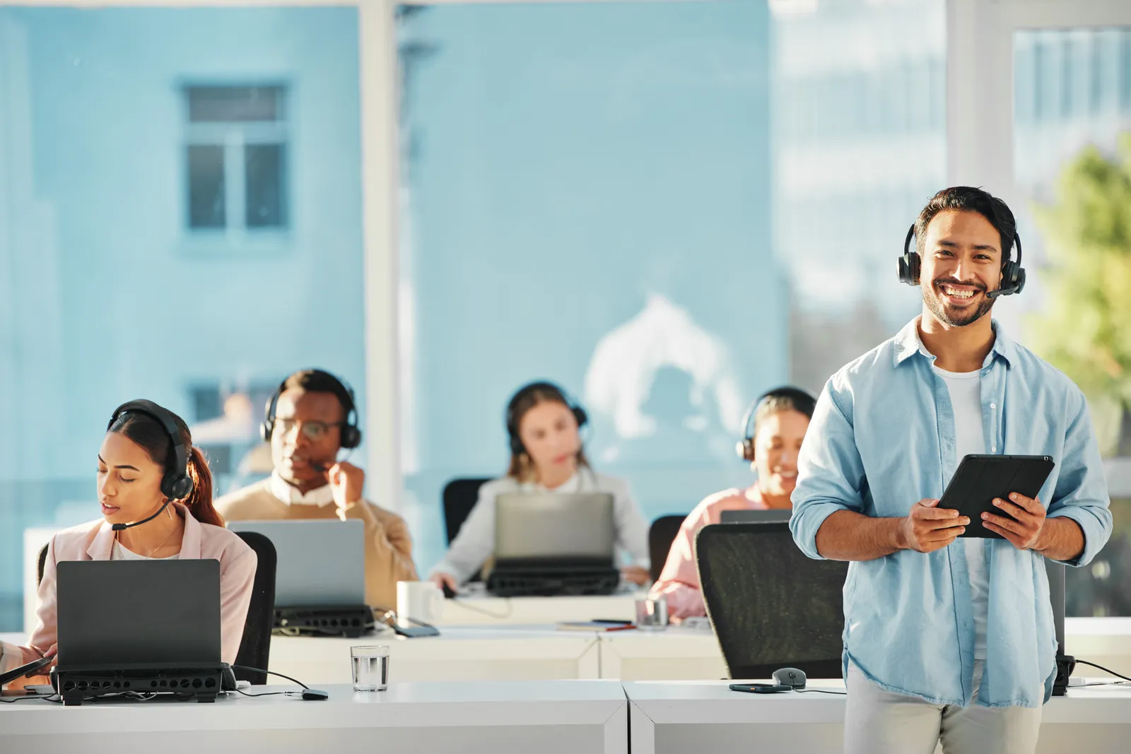 A group of call reps sitting at their desk while their manager stands in front of them smiling.