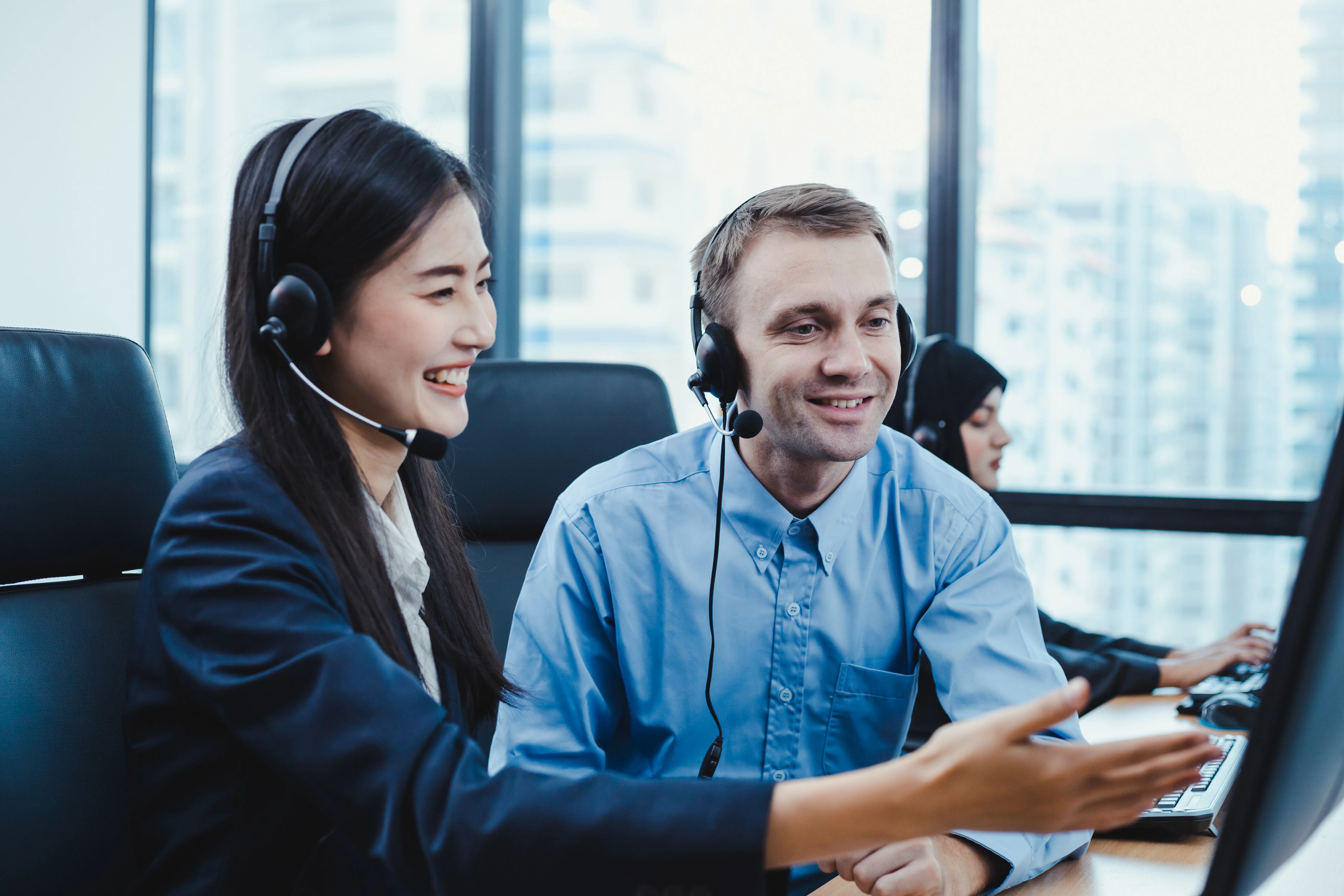 Two coworkers at a call center. One is gesturing to the screen and coaching her coworker.