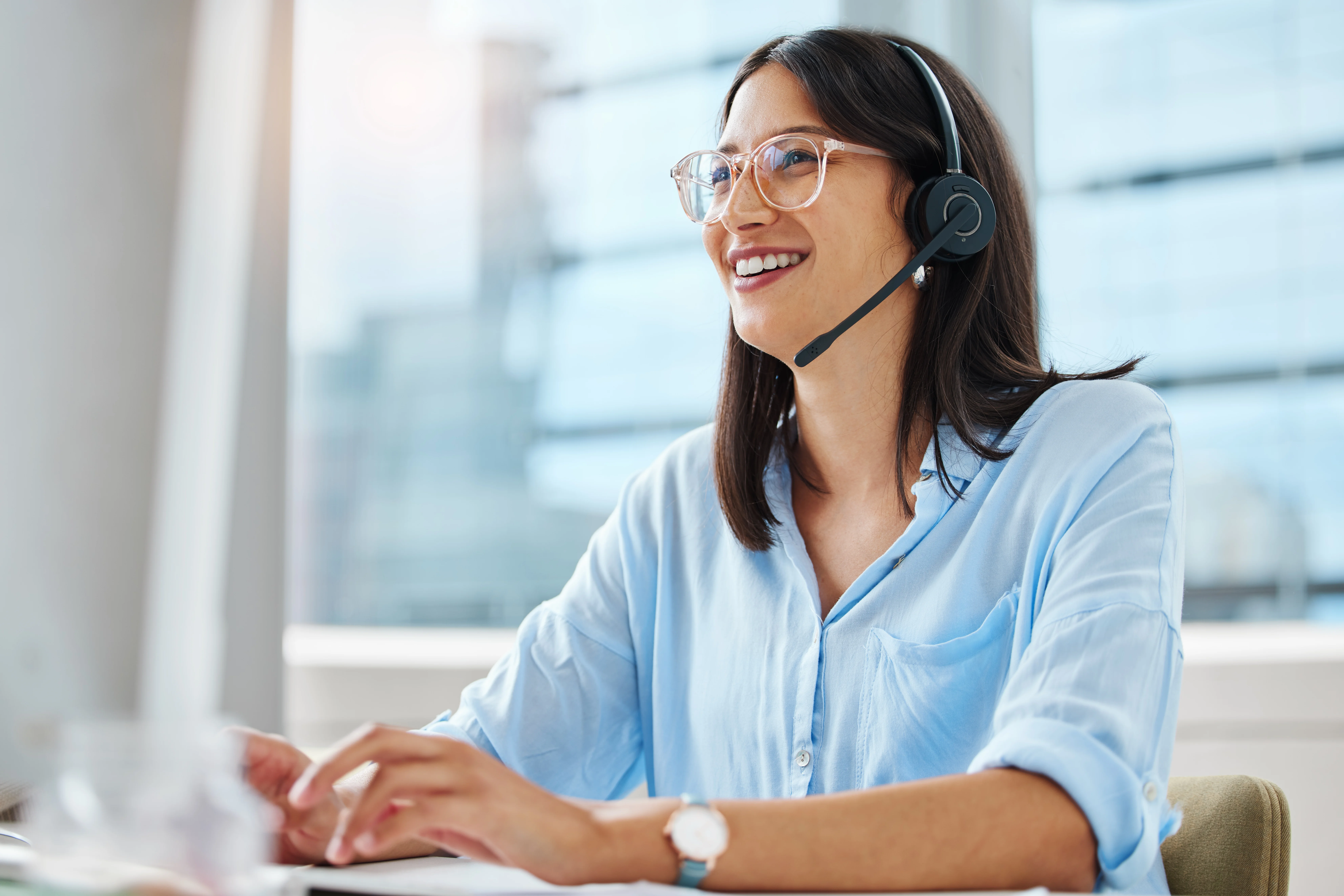 A woman wearing a headset smiling at a computer screen.
