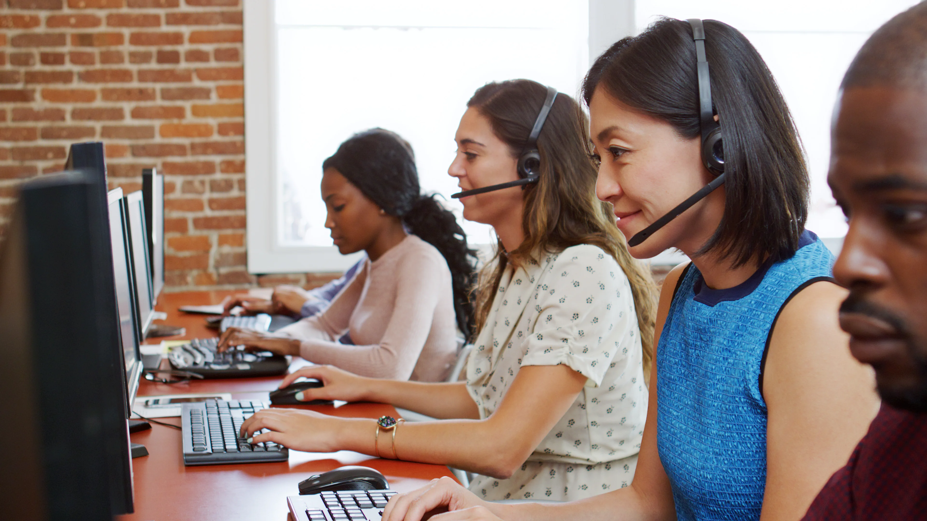 A group of call center representatives wearing headsets and looking at their computers.