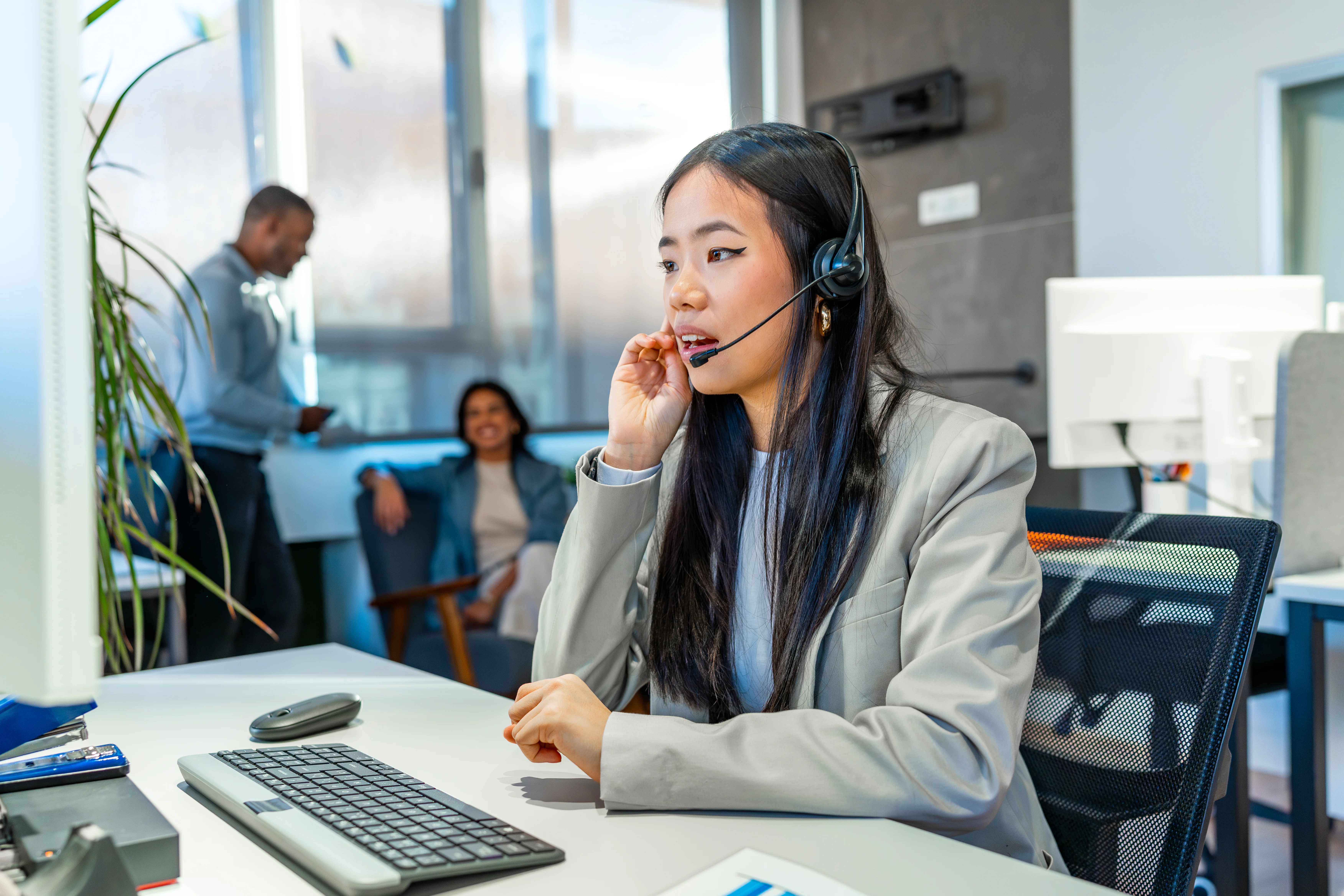 A woman wearing a headset looking at a computer. She has a serious expression on her face.