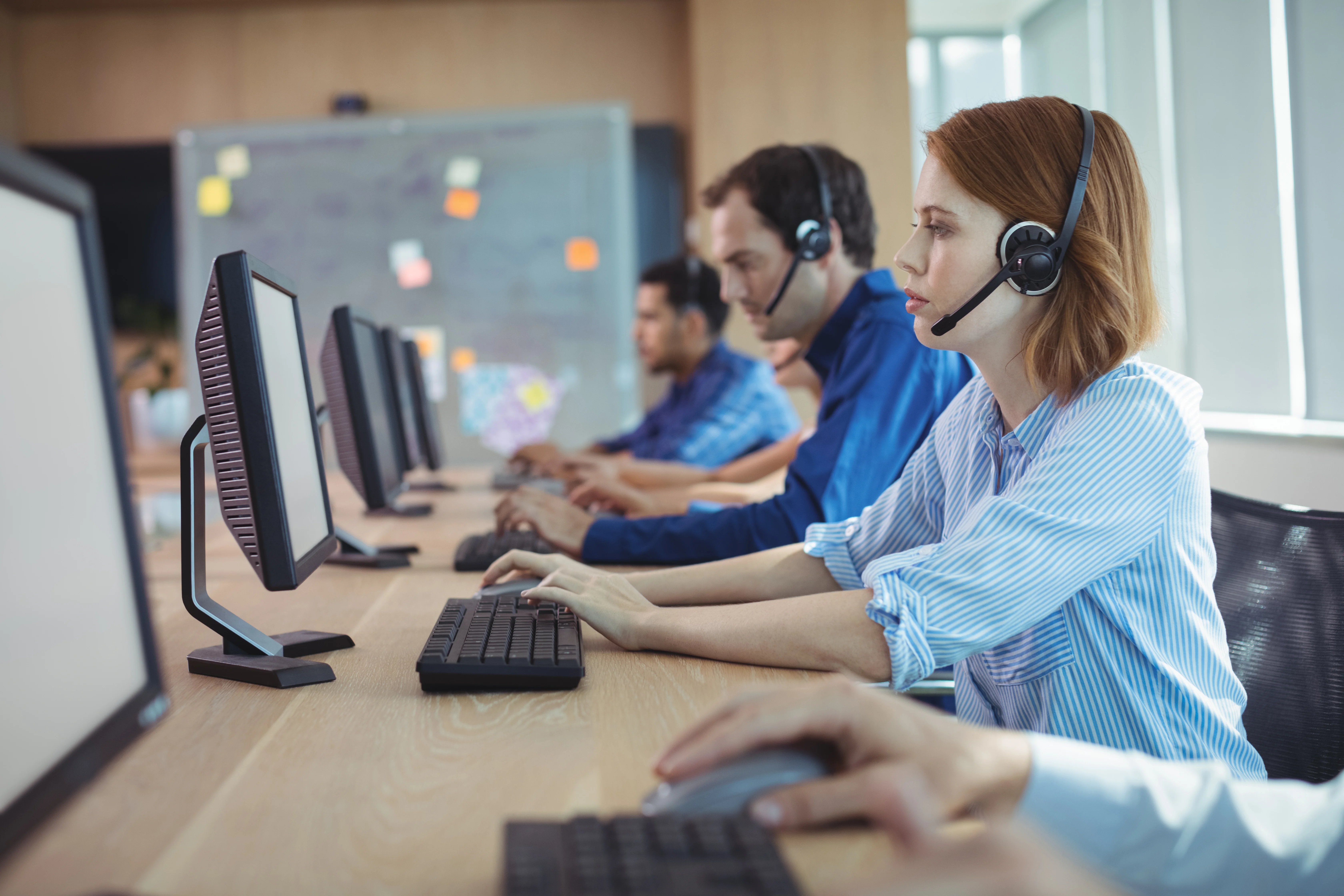 A group of people at a call center. The focus is on a woman wearing a headset and looking at her screen.