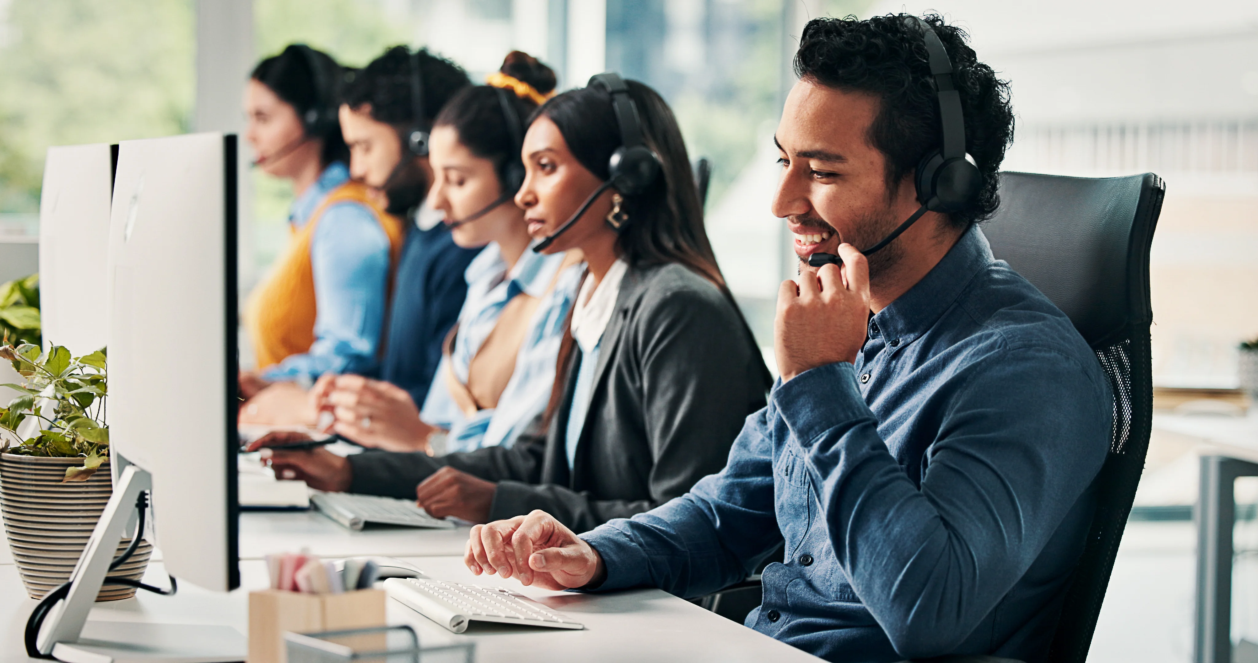 A group of call representatives sitting at a desk. The focus is on a man who is holding his headset.