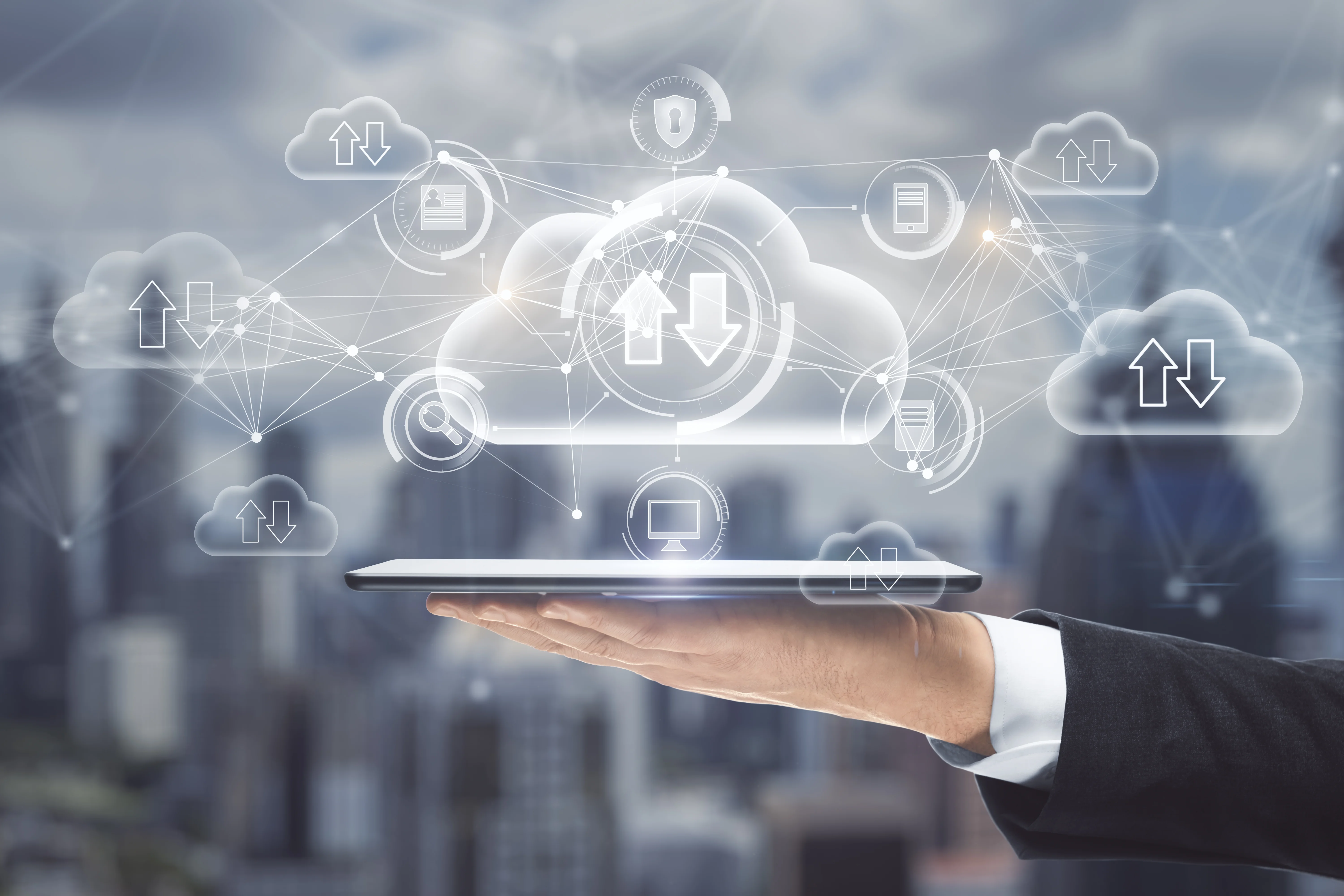 A man holding a tablet up. Above the tablet, there are several icons of clouds with up and down arrows and other images surrounding the cloud symbolizing a cohesive system.