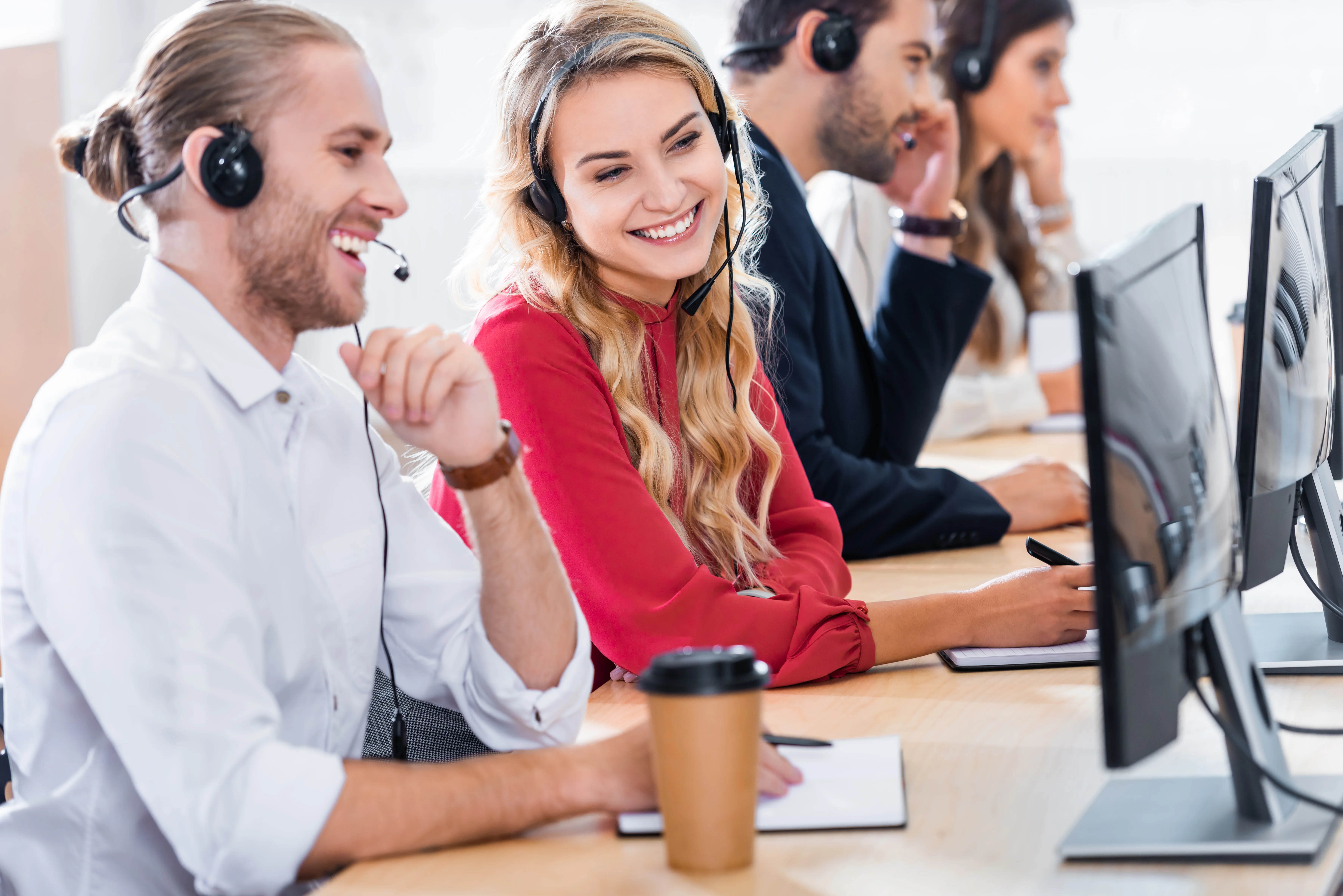A group of coworkers looking at a screen and smiling. They are all wearing headsets with notebooks in front of them.