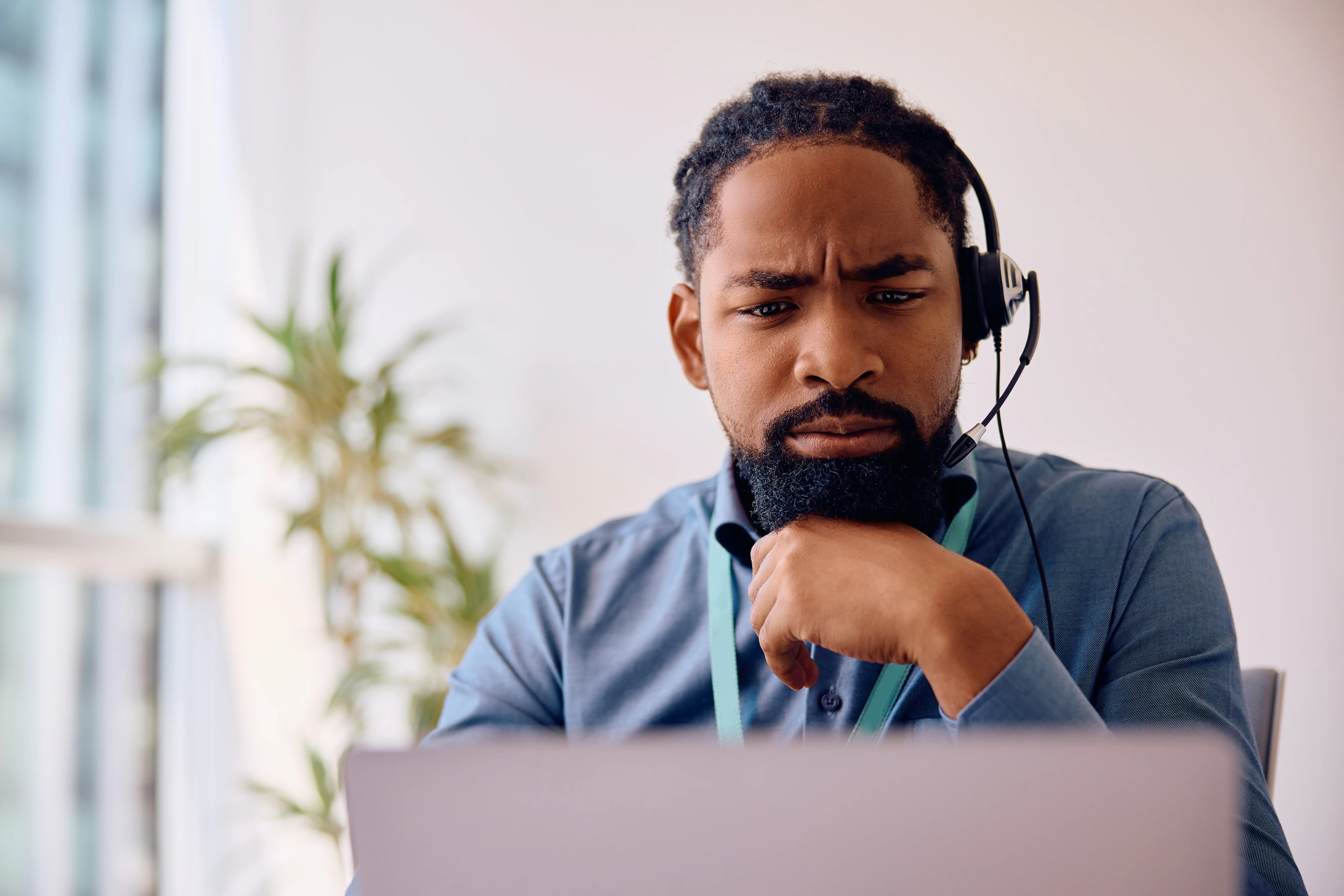 A call representative wearing a headset. He is looking puzzled while looking at his computer monitor.