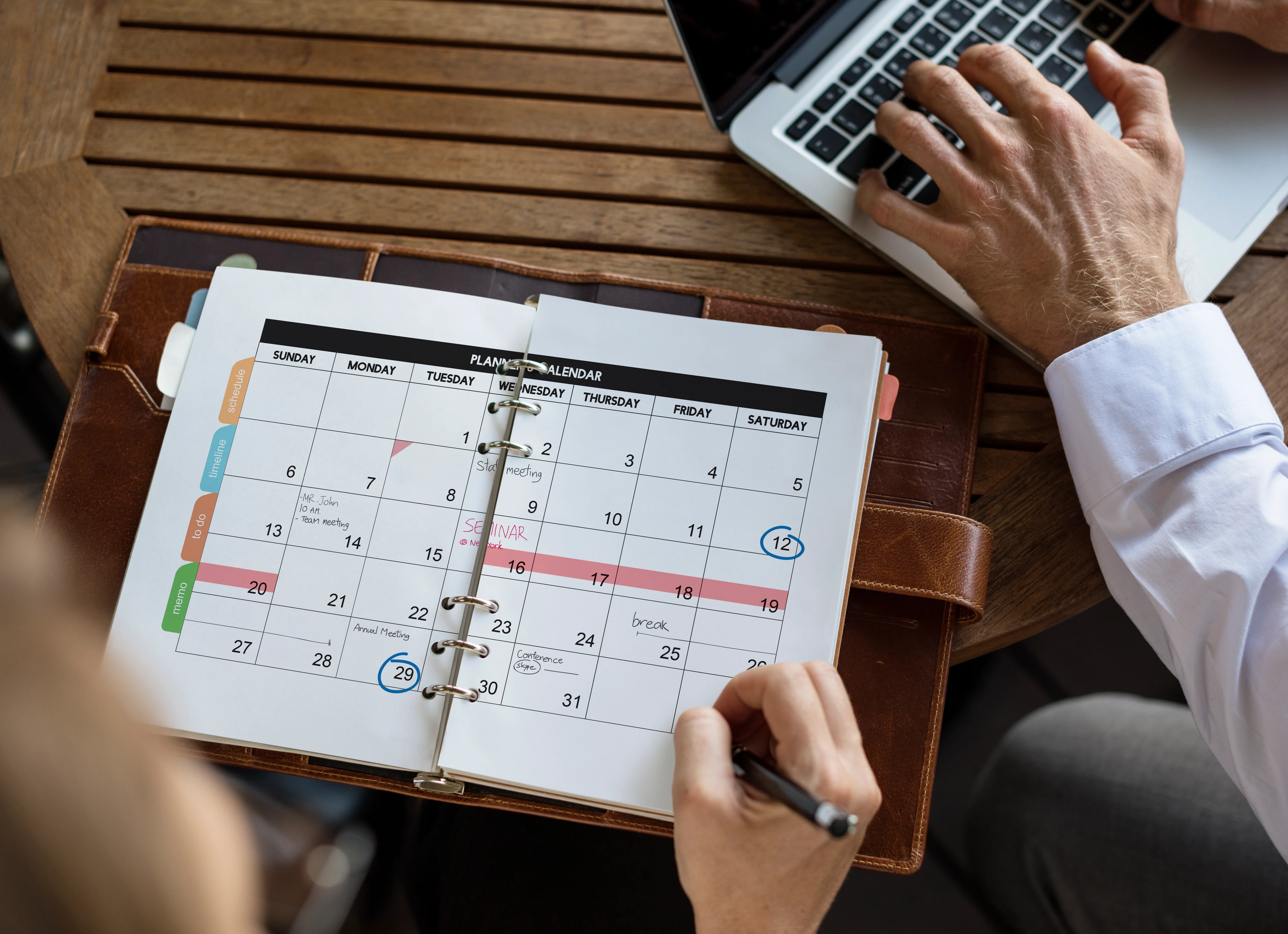 A person organizing their schedule. Next to them is a man working on his computer.