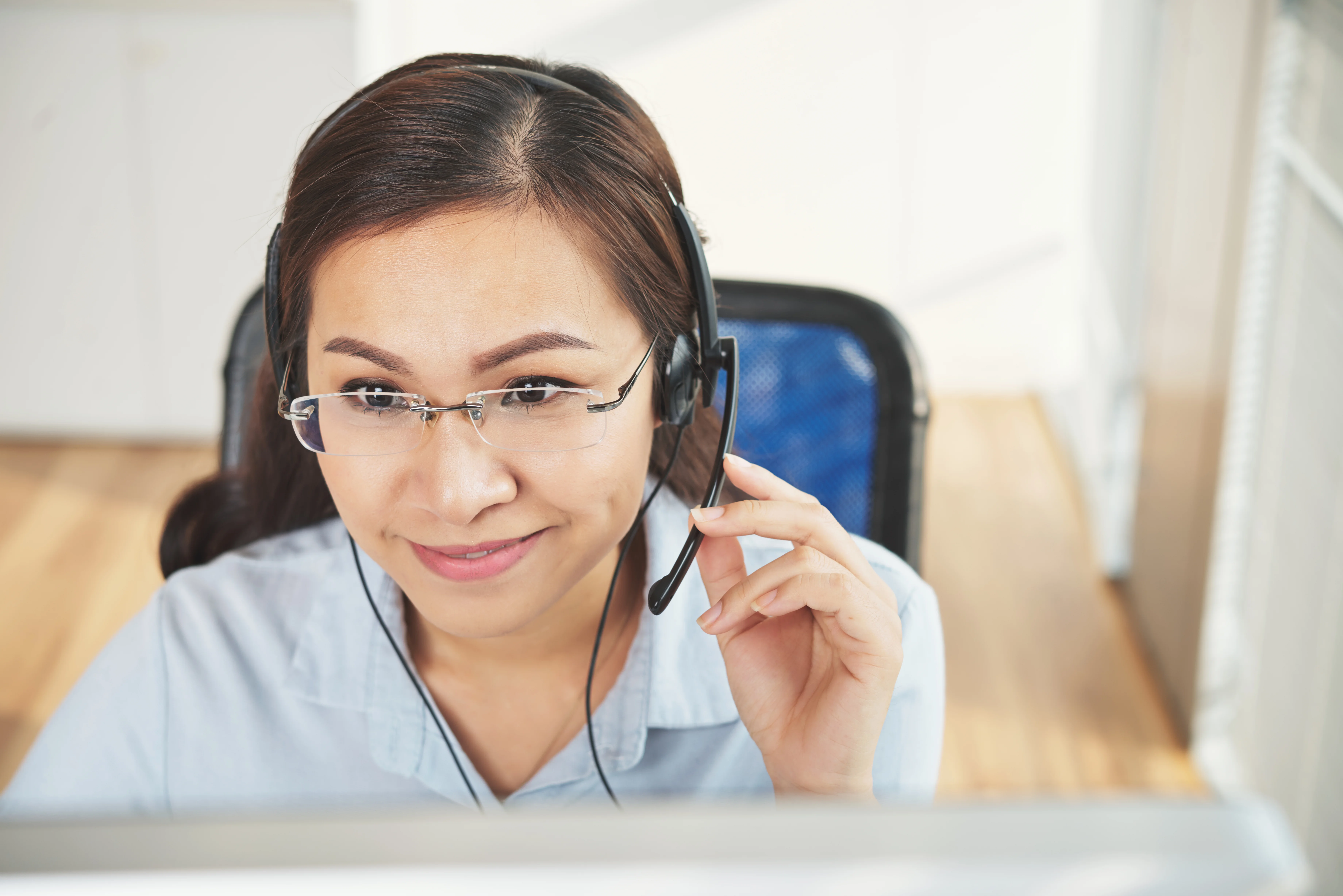 A woman alone at her home office. She is using a headset and smiling at her computer screen.