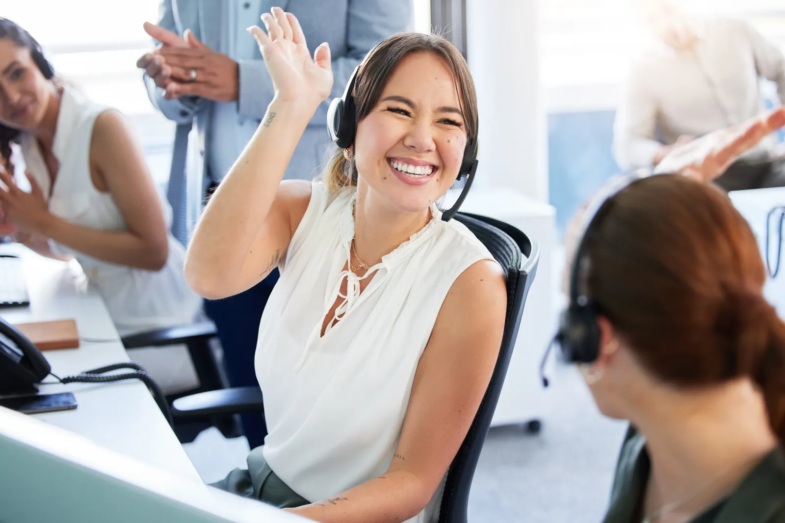 A woman high-fiving her coworker. Other coworkers are around them clapping.
