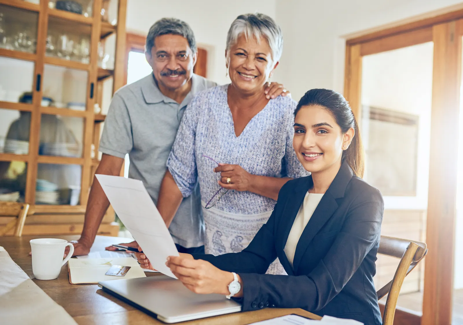 A life insurance agent holding a policy with a senior couple standing next to them.