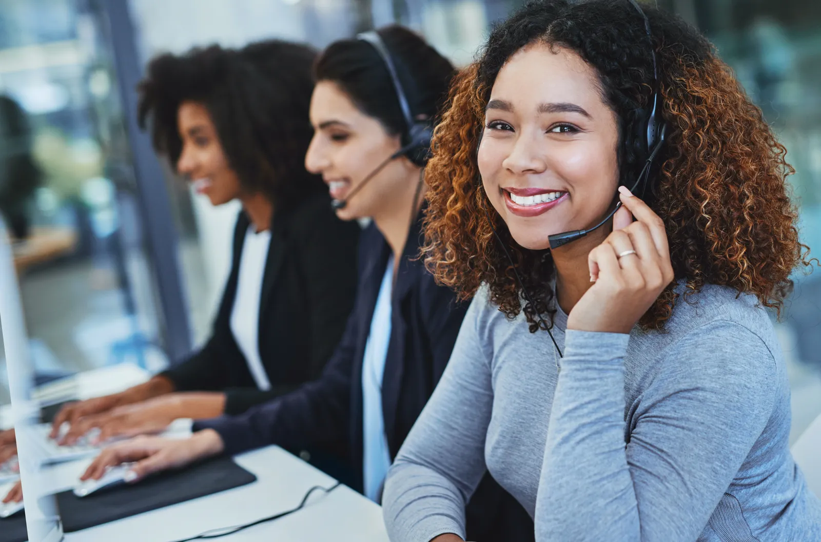 A group of woman sitting in a modern office. One of them is smiling at the camera.