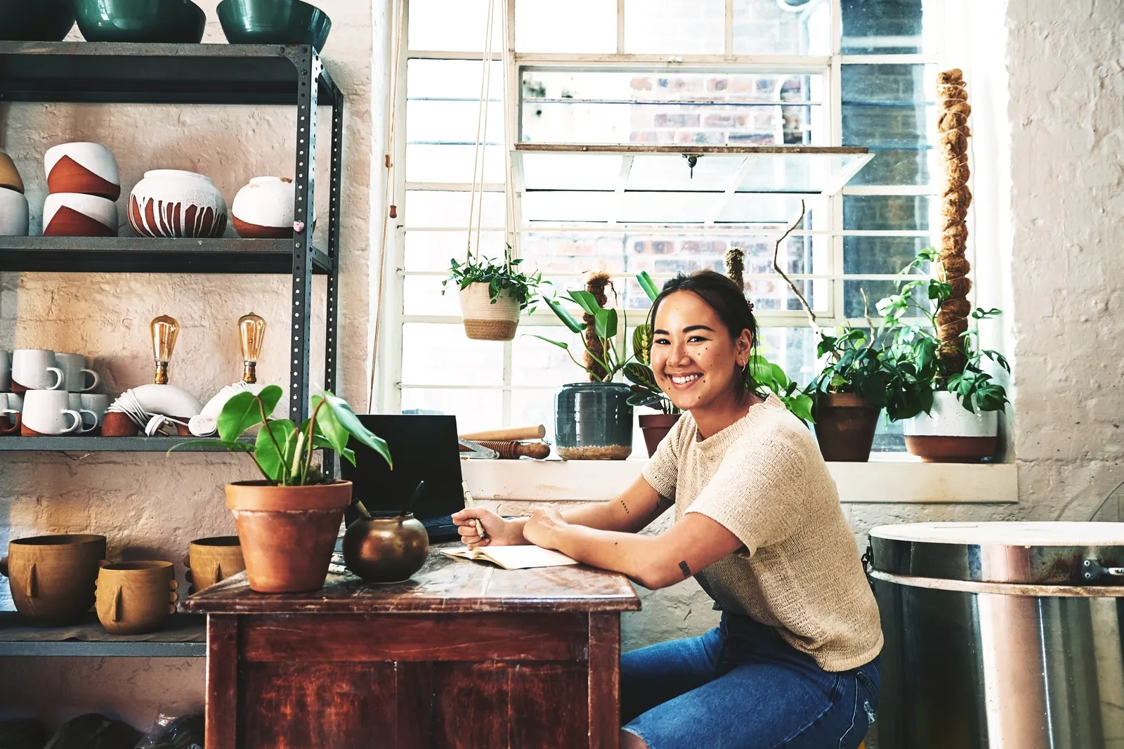 A smiling woman sitting at a desk with a computer and notebook in front of her.