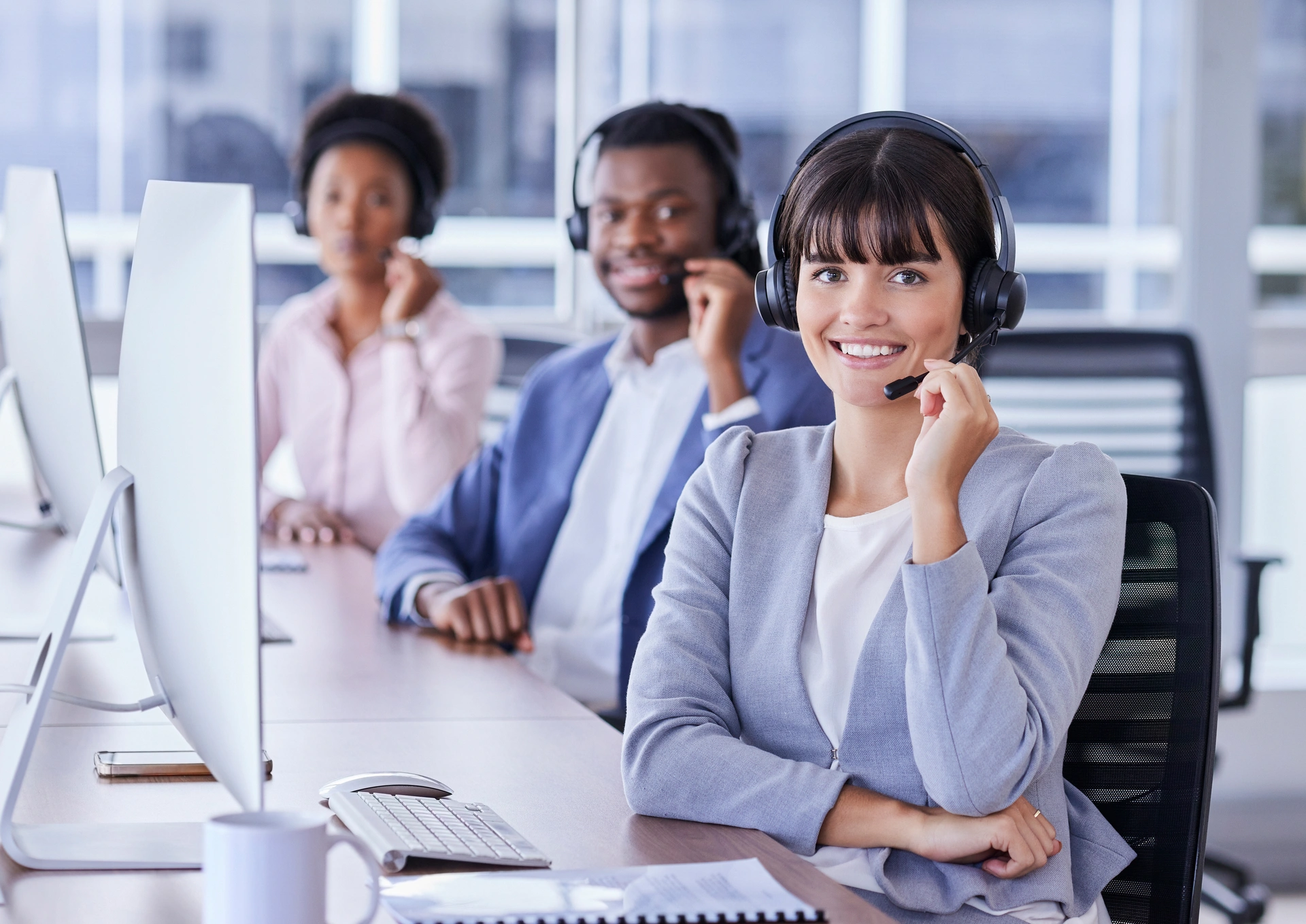 A group of call center agents. They are all looking into the camera and holding onto the mics on their headsets.