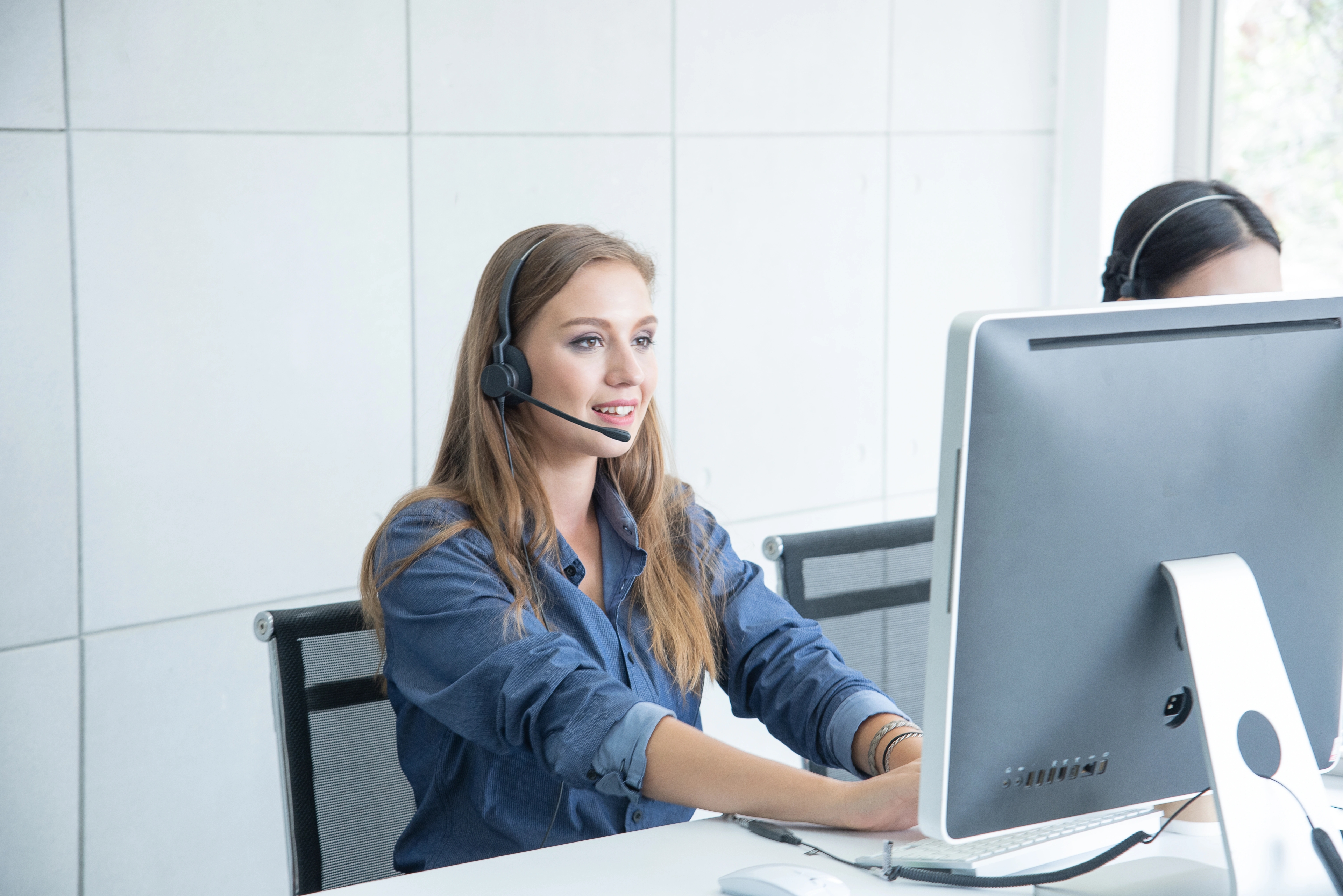 A woman using a computer while on a headset.