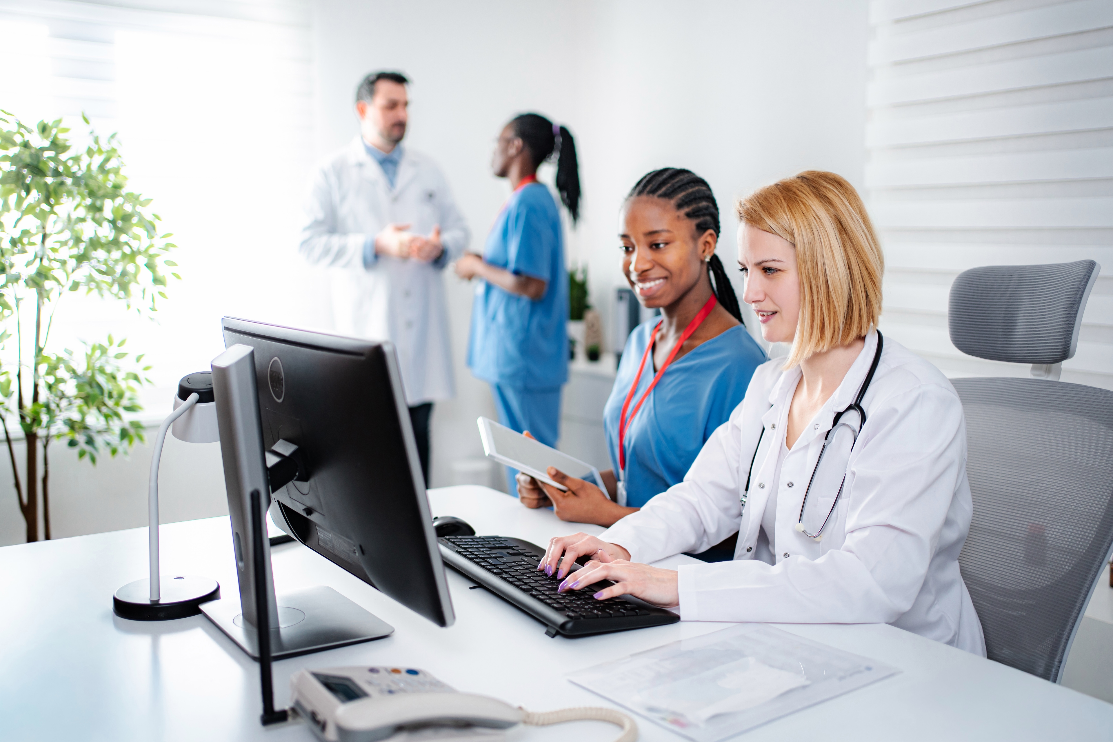 A doctor and nurse looking at a computer monitor. The doctor has her hands on the keyboard, while the nurse is holding an iPad.