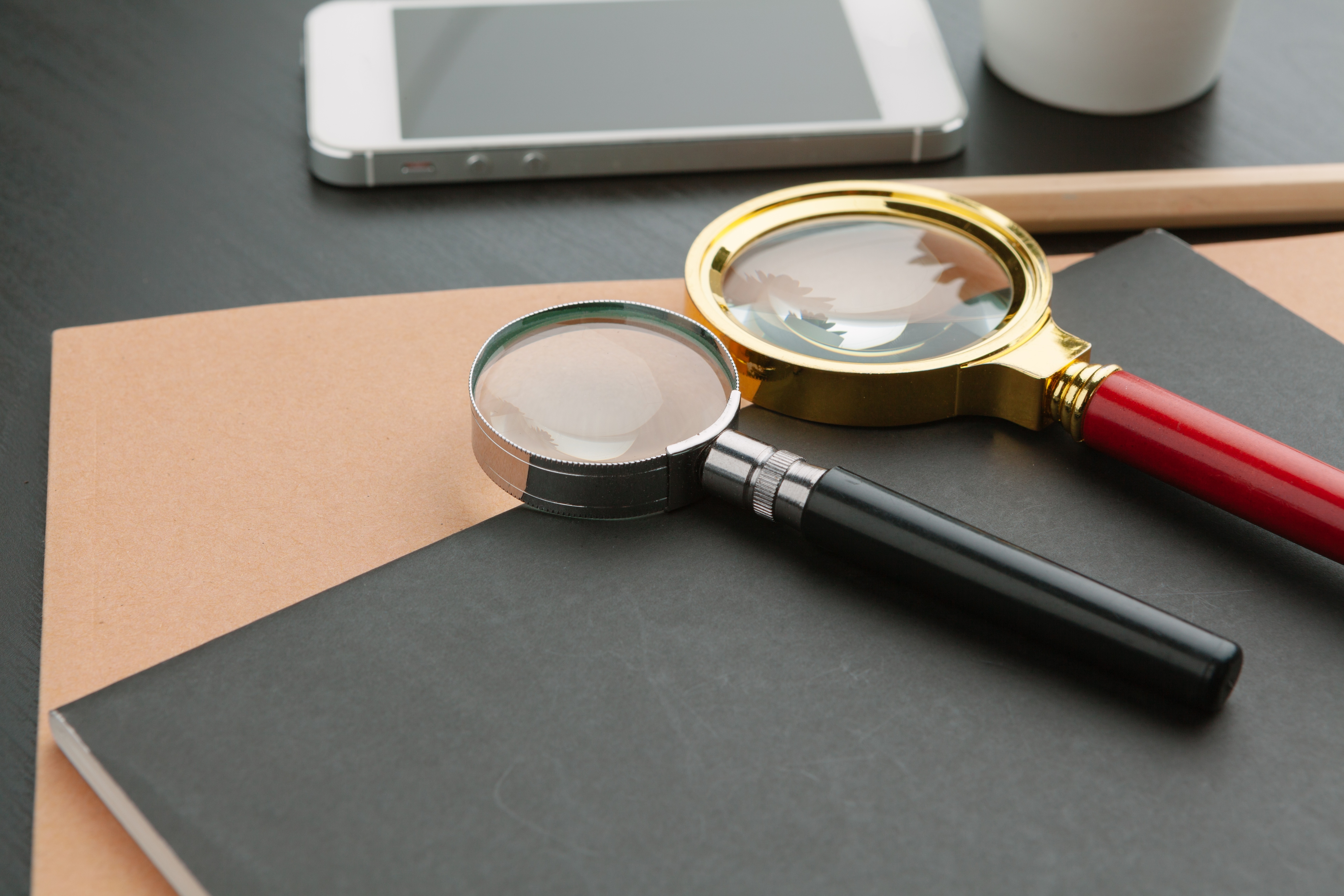 Two magnifying glasses on top of a notebook on a desk. There is a phone in the background.