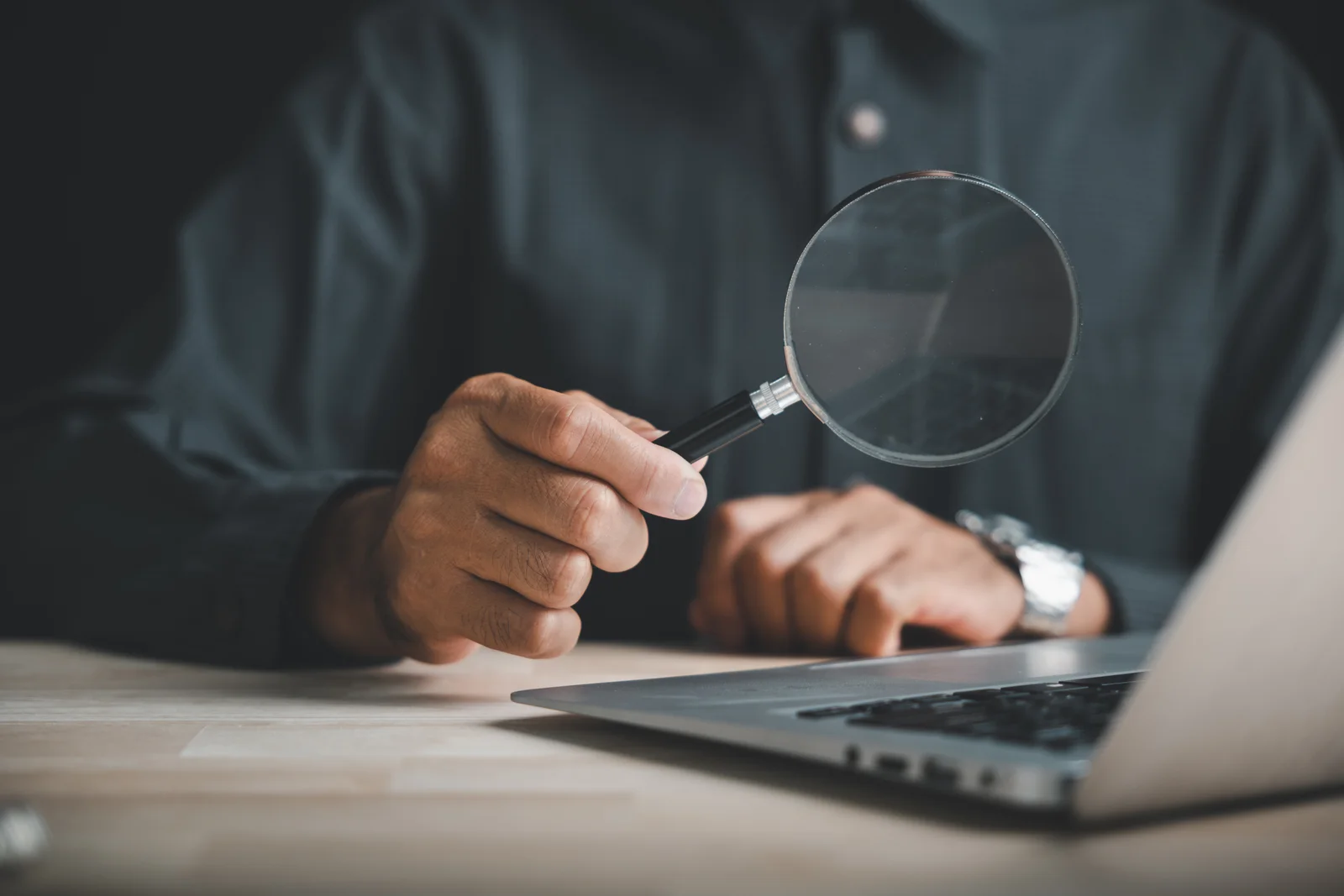 A man using a magnifying glass to look at his computer.
