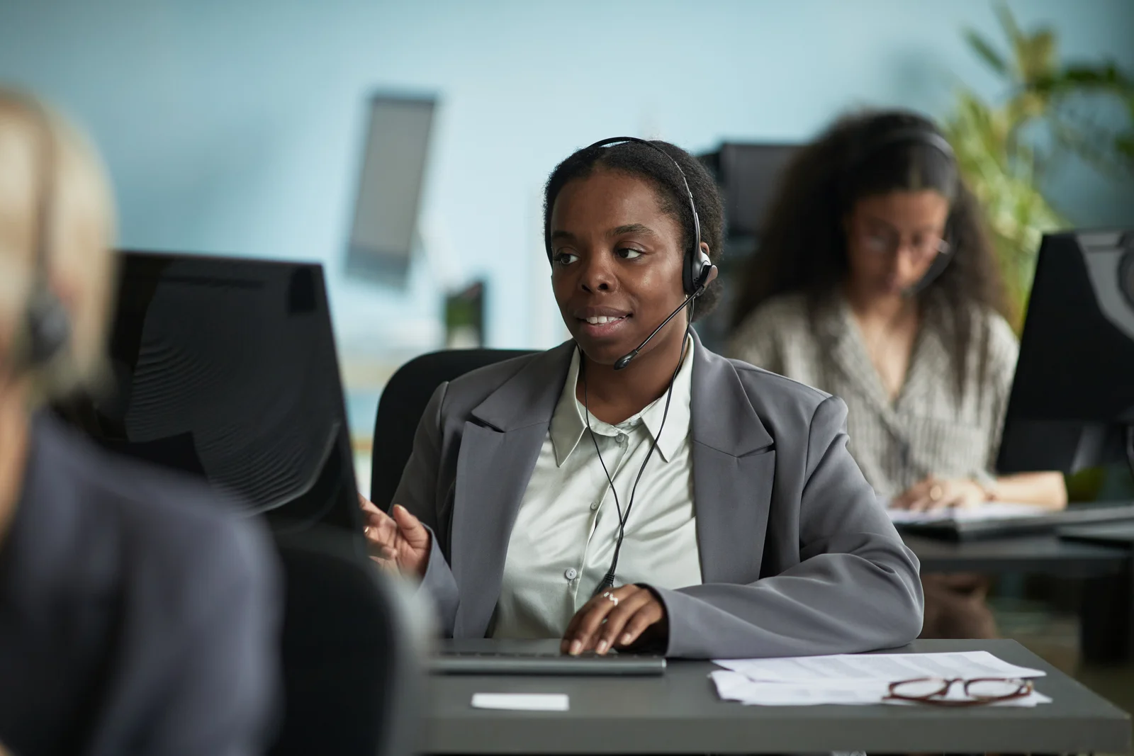 A young woman in a blazer with a headset on. She seems to be talking to the person on the headset.