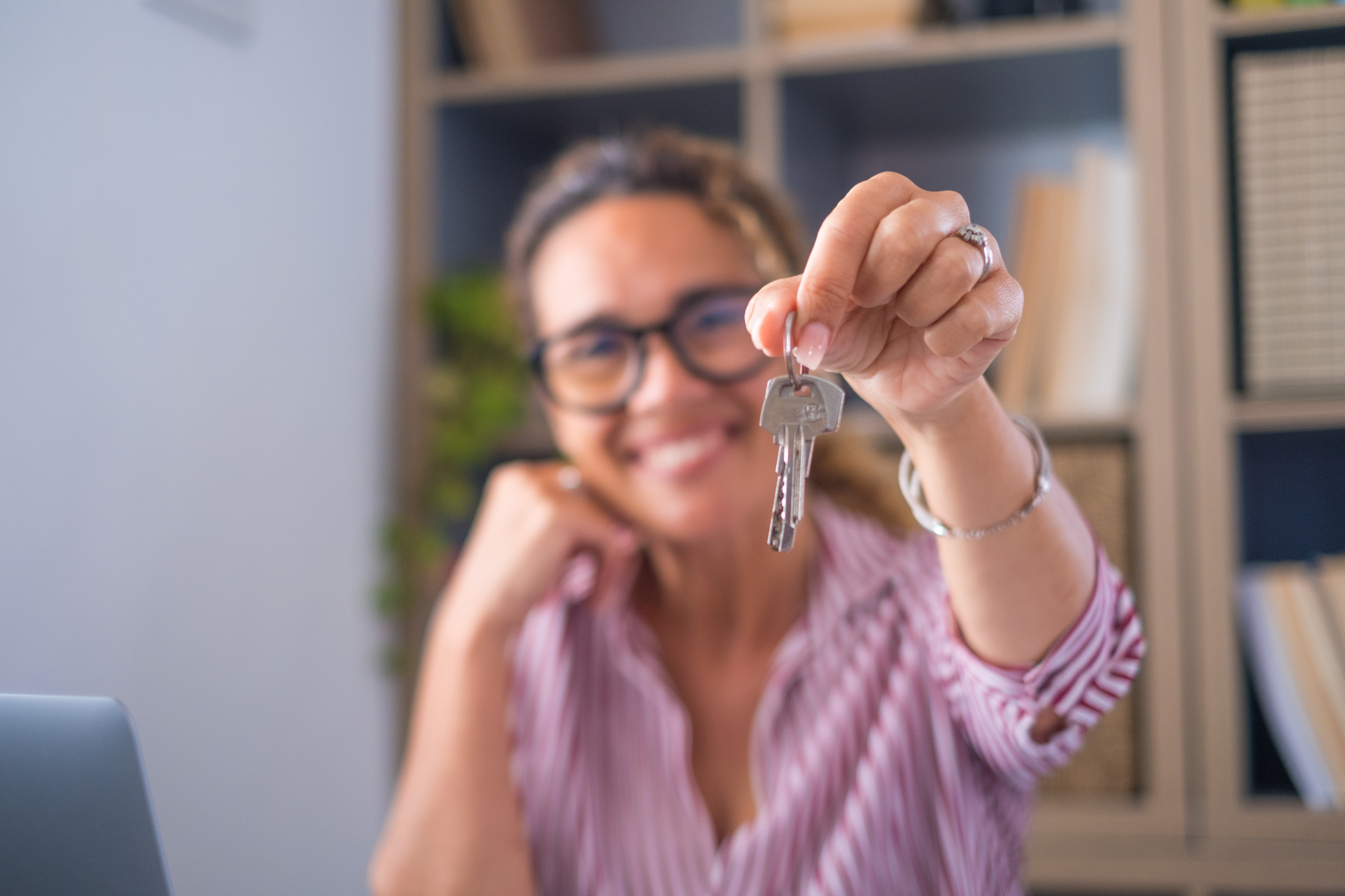 A woman holding up a pair of keys in a home office. She is sat in front of a computer.