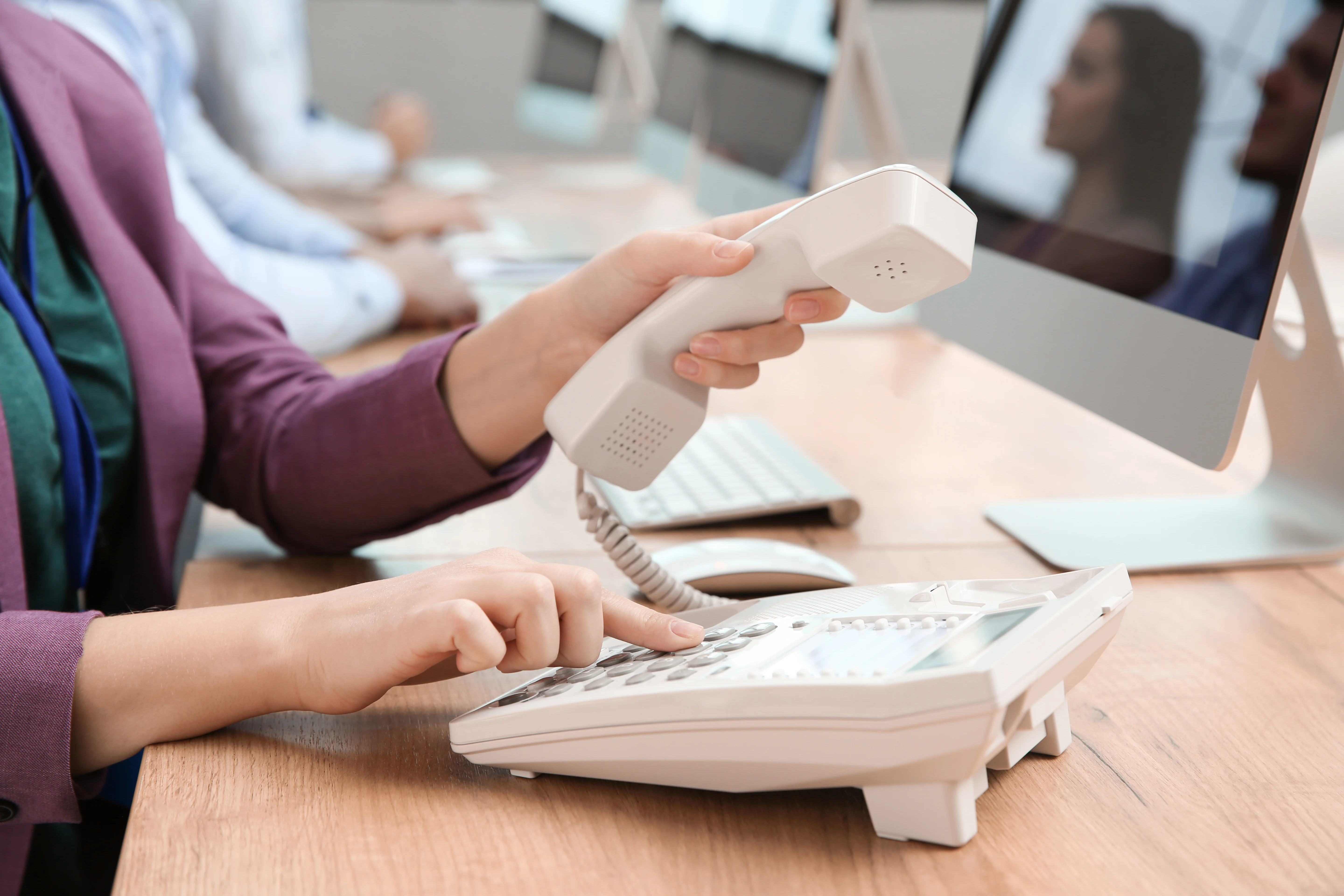 A person using a traditional phone to call someone. They are sat in front of a computer.