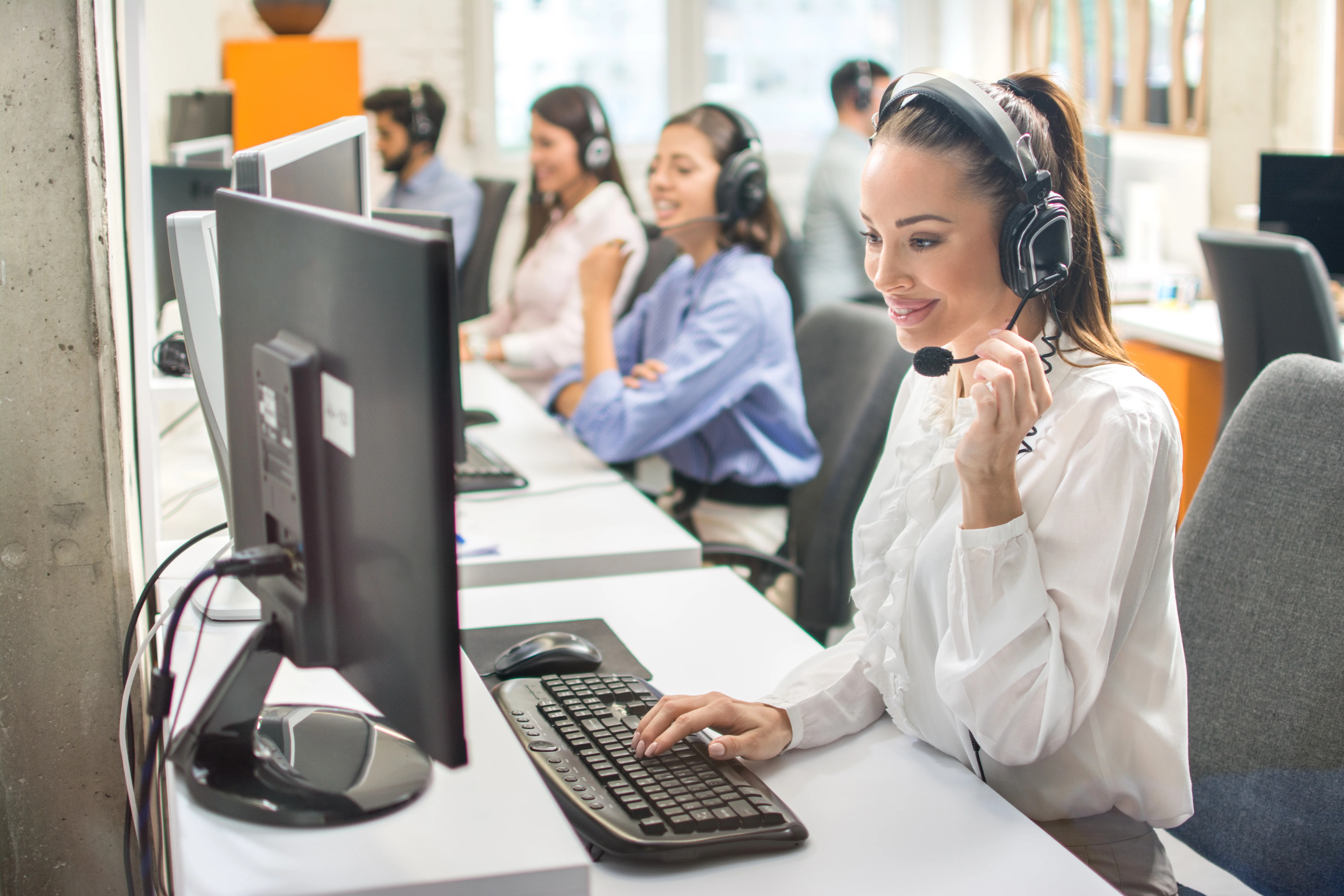 A woman using her headset and computer to make a call using a virtual phone number.