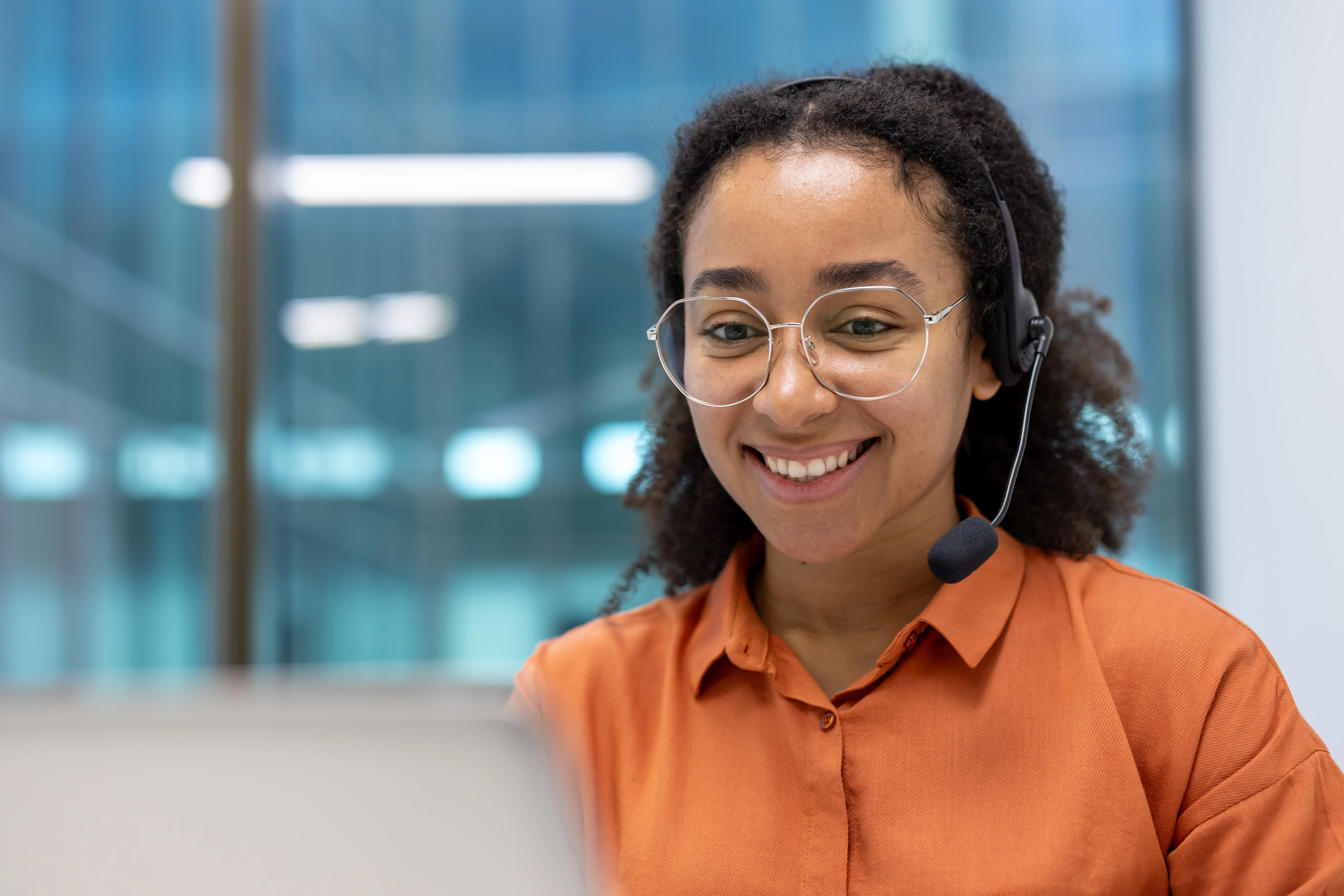 Smiling woman wearing a headset. She is staring at a computer.