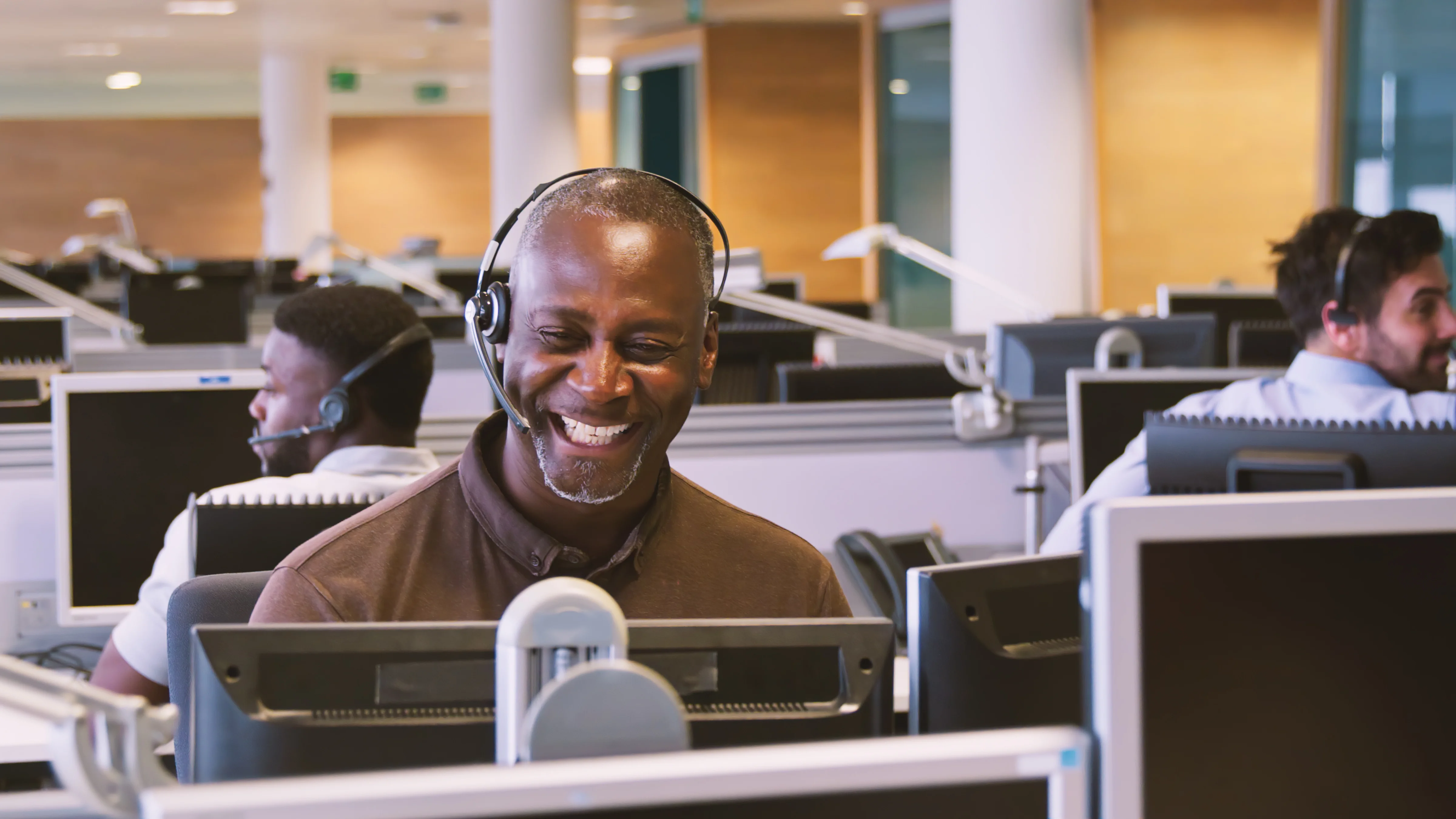 A smiling man wearing a headset looking at his computer.