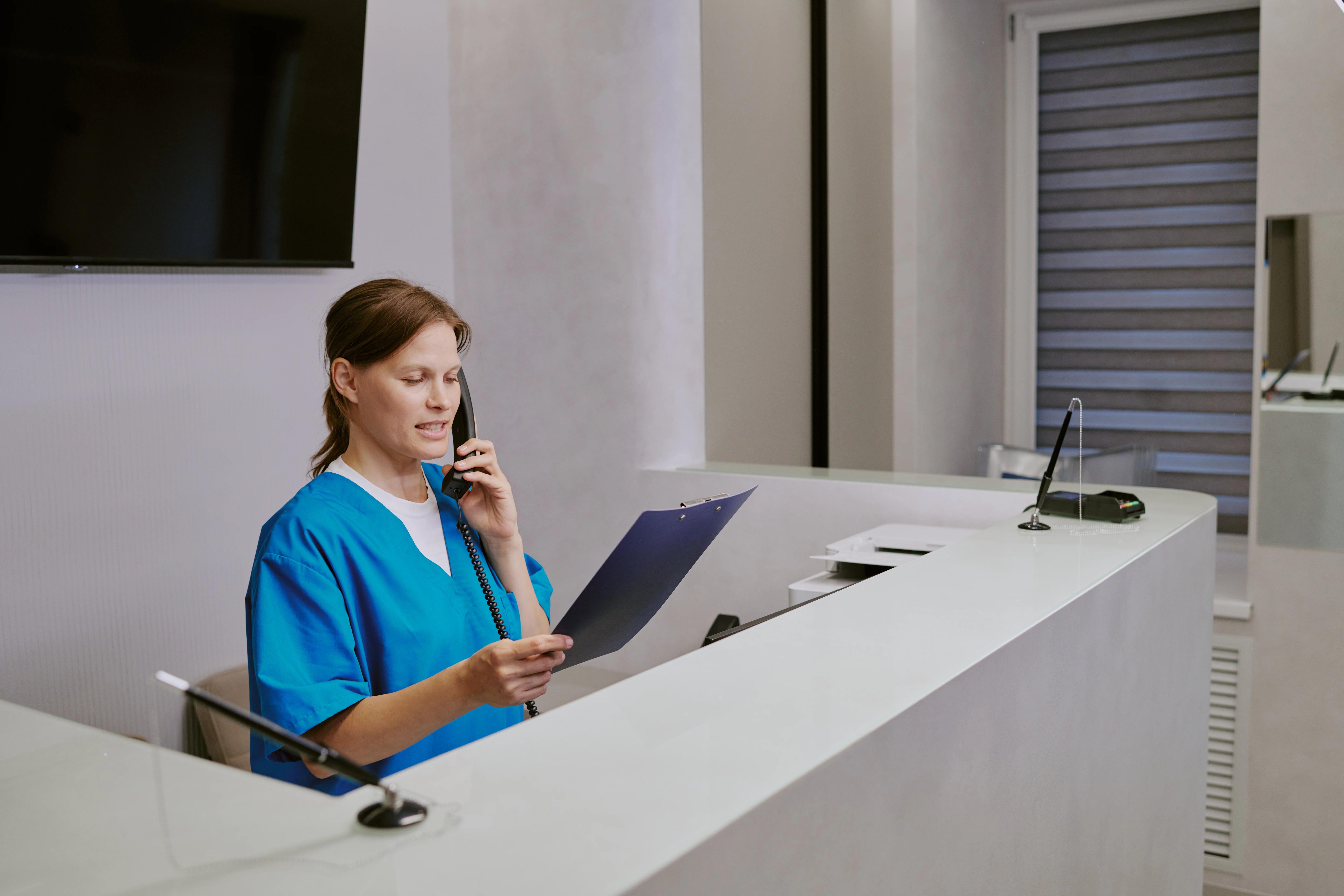 A woman wearing scrubs answering the phone while holding a chart.